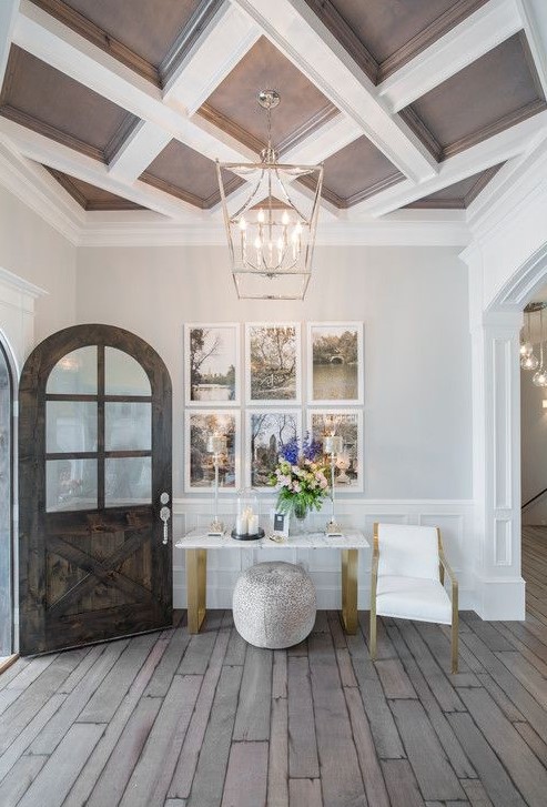 a refined entryway with paneling on the walls, a console and a chair, a gallery wlal, a coffered taupe and white ceiling, a lovely chandelier