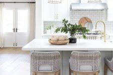 a romantic coastal kitchen with dove grey and white cabinetry, a large kitchen island with a meal space, grey stools and glass lamps