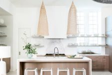 a serene coastal kitchen with stained cabinets, a large wooden kitchen island, statement wicker lamps, wooden beams and wicker chairs