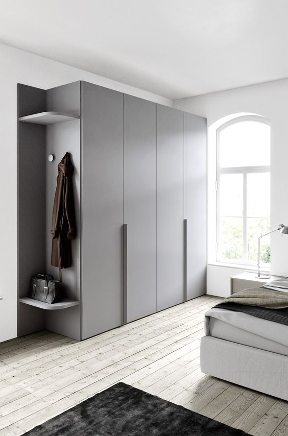 a sleek Scandinavian bedroom with an upholstered bed, neutral bedding, a large sleek wardrobe, table lamps and arched windows