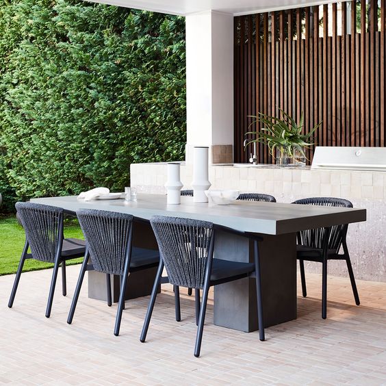 a sleek and elegant outdoor dining space with a metal and concrete table and metal black chairs plus candles and greenery