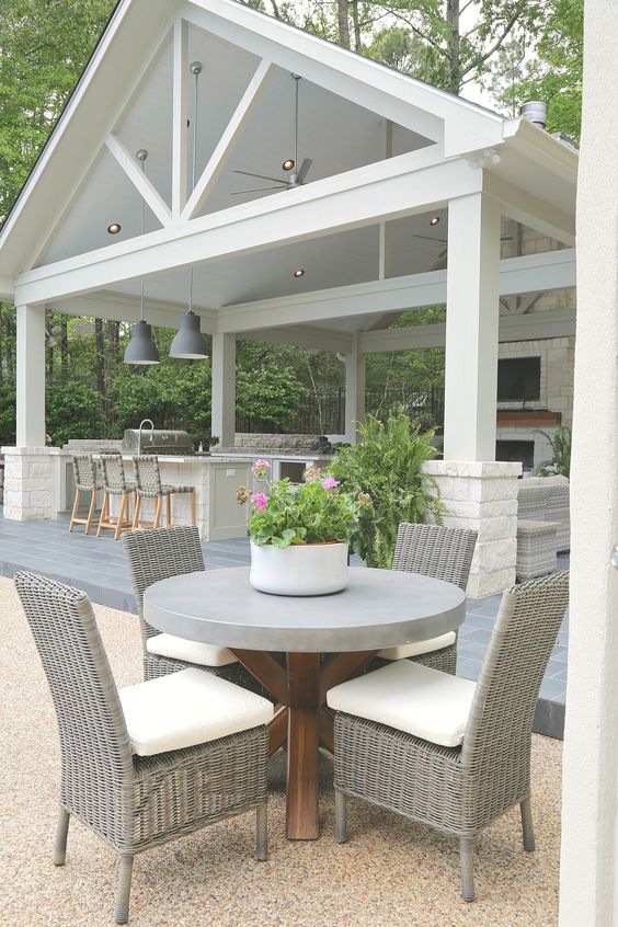a sleek and neutral modern outdoor space with a round concrete table, wicker chairs and a white outdoor kitchen plus pendant lamps