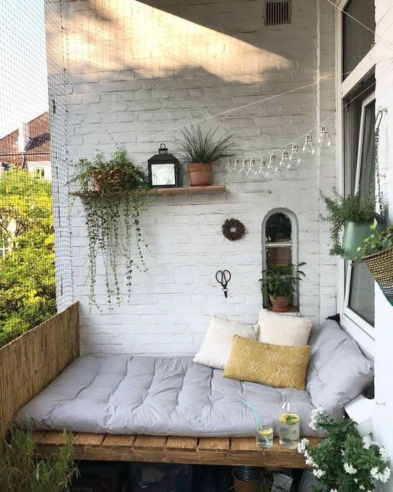 a small balcony bedroom with a pallet bed with lots of pillows, potted plants and lights over the space is cool