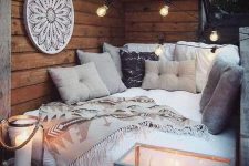 a small boho balcony bedroom with a low bed with lots of pillows, a dream catcher and lots of candles around