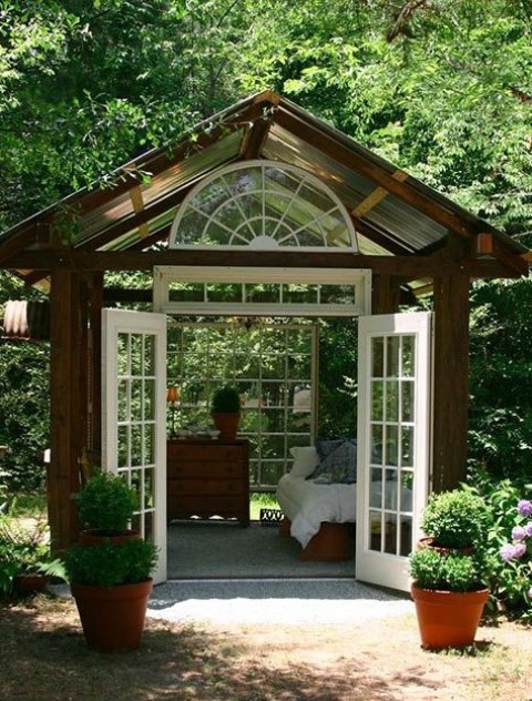 a small wood and glass garden house with comfortable vintage furniture and garden views is a lovely outdoor bedroom