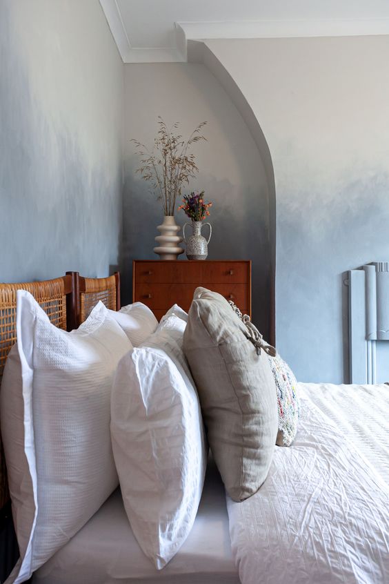 a soothing and chic bedroom with ombre grey walls, a niche with a dresser, a bed with a woven headboard and neutral bedding