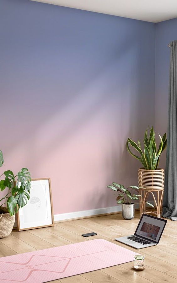 a soothing space with a lilac and pink gradient wall, a pink yoga mat, some potted plants and artwork