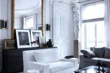 a sophisticated Parisian-inspired living room with white walls and a ceiling detailed with refined molding, with simple white furniture and a mini gallery wall plus an oversized mirror