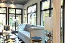 a sophisticated space with a series of windows, an elegant sofa, black and gold chairs and a lovely tin tile ceiling