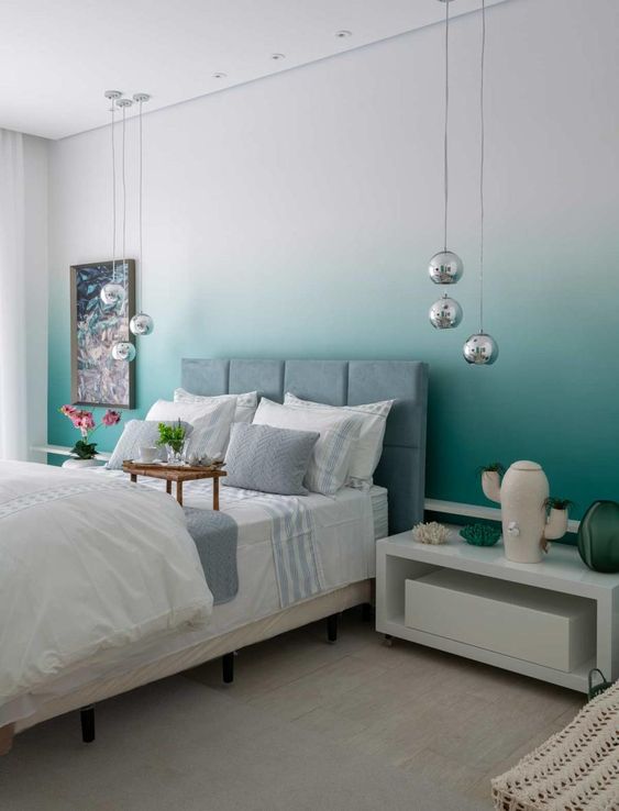 a stylish and bold bedroom with an ombre green accent wall, a grey upholstered bed, neutral bedding, pendant lamps and white nightstands