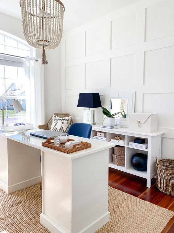 a stylish beach home office with white paneling, white furniture, navy accents, baskets and a wooden bead chandelier is gorgeous