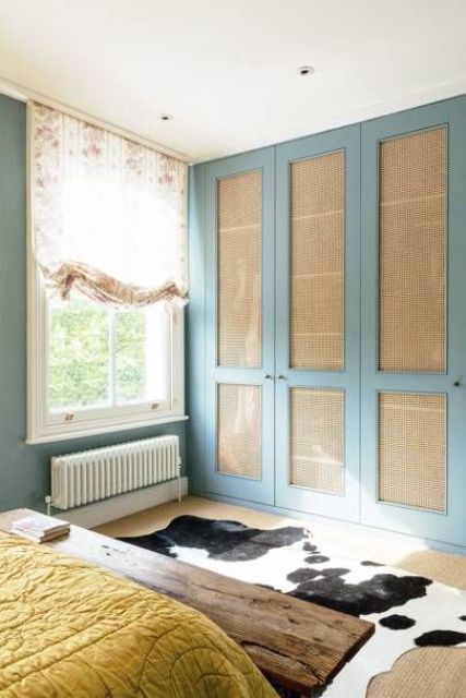 a stylish bedroom with blue walls, built-in wardrobe with blue and natural cane doors, a bed and a stained bench, a cowhide rug is wow
