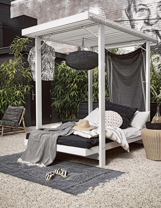 a stylish black and white bedroom with a white canopy bed with black and white bedding, a black woven lamp and a woven nightstand plus a rug