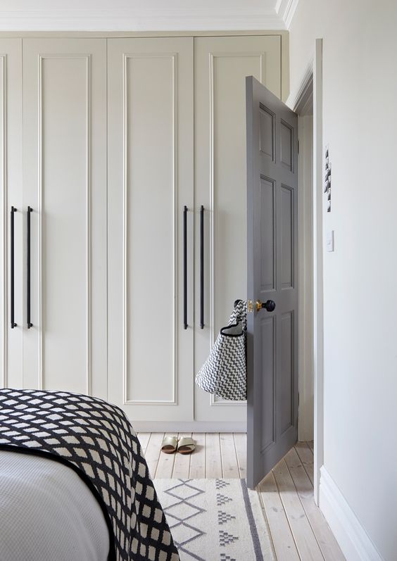 a stylish neutral bedroom with creamy wall-to-wall wardrobes, a bed with black and white bedding and a printed rug is a cool and bold idea