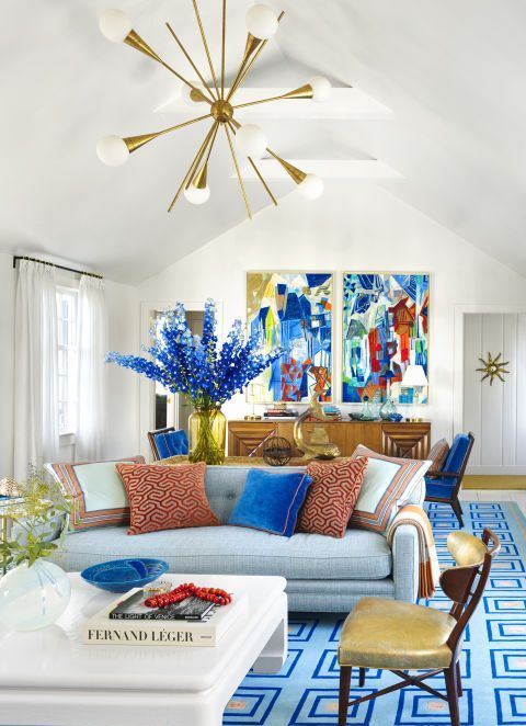 a super bold living space with bright artworks, blooms, a blue printed rug, printed pillows is a fun and bold summer space