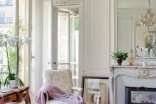 a super refined vintage French living room with a non-working fireplace, molding on the walls and ceiling, a blush chandelier and sophisticated furniture