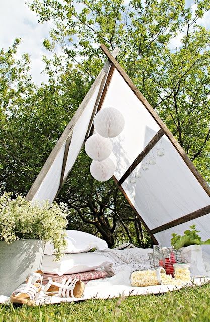 a teepee in the garden turned into a small bedroom with lots of pillows and blankets, potted greenery and paper pompoms