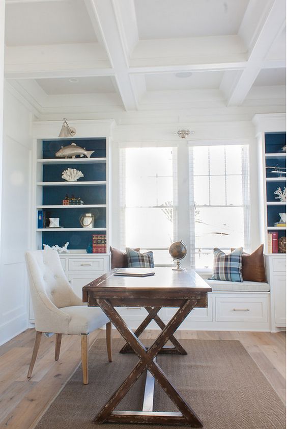 a traditional beach home office with white storage units and a built-in daybed, a trestle desk, an upohlstered chair and sea-themed decor