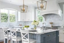 a vintage coastal kitchen is given a coastal touch with a pale blue kitchen island, a chic look with brass touches and a vintage feel with white stools