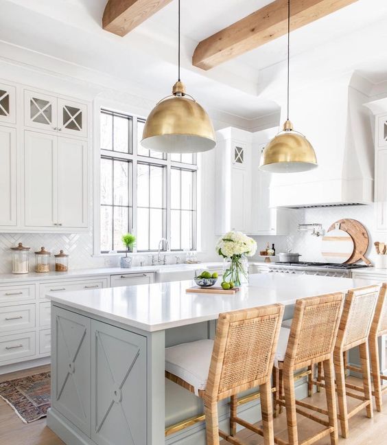 a vintage infused coastal kitchen with white cabinetry, a light blue ktichen island, rattan stools and gold pendant lamps