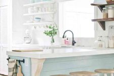 a vintage-inspired coastal kitchen with white cabinets, a light blue kitchen island and matching lamps over it, open shelving and vintage stools