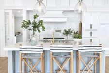 a vintage-inspired coastal kitchen with white cabinets, a light blue kitchen island, striped stools and glass pendant lamps