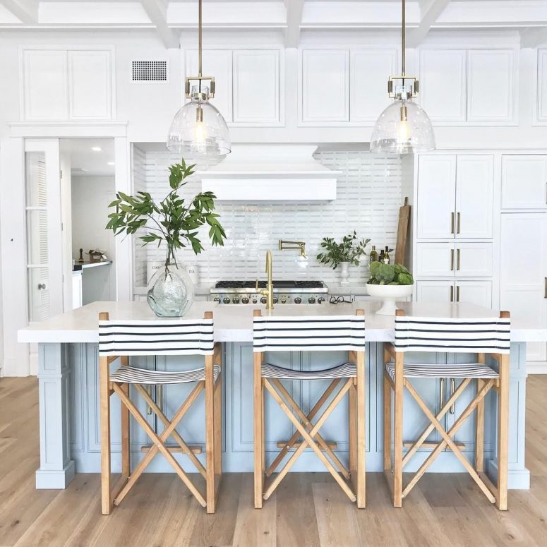 a vintage inspired coastal kitchen with white cabinets, a light blue kitchen island, striped stools and glass pendant lamps