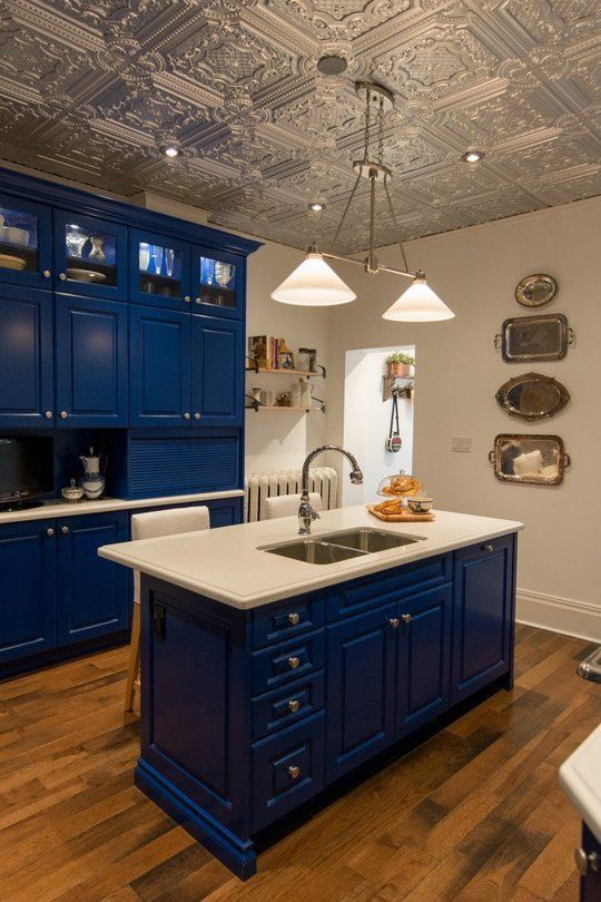 a vintage kitchen with a tin tile ceiling, bold blue cabinets, white countertops, a pendant lamp and a gallery wall