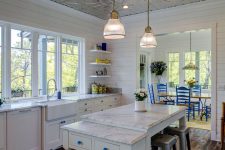 a white farmhouse kitchen with a beautiful tin tile ceiling, white cabinets, a kitchen island and metal stools, pendant lamps