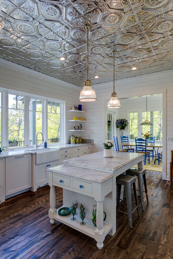 a white farmhouse kitchen with a beautiful tin tile ceiling, white cabinets, a kitchen island and metal stools, pendant lamps