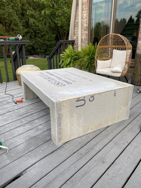 a wooden deck with a rattan chair and a large concrete table with prints and potted ferns is a cool and welcoming space