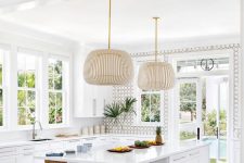 an airy and vivacious neutral beach kitchen with white shaker cabinets, an accent wall, a kitchen island with a dining space and catchy pendant lamps