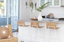 an inspiring beach kitchen with white cabinets, a kitchen island, woven pendant lamps, wooden sotols, a wicker chair and a matching tray