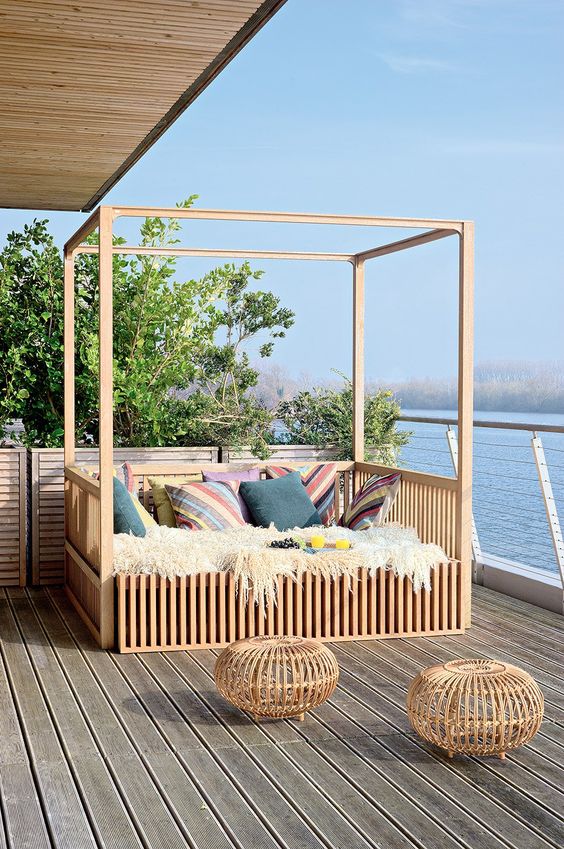 an outdoor bedroom on the terrace, next to the water, with a large framed bed with lots of colorful pillows