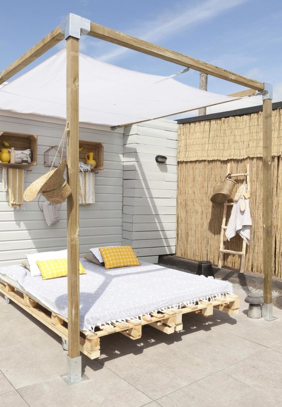 an ultimate coastal outdoor bedroom with a bed feturing a canopy over it, some pillows, crates as storage shelves and a ladder