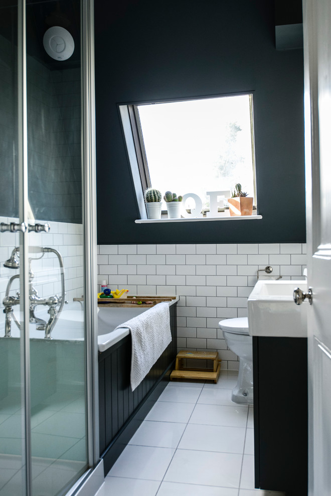 a small elegant attic bathroom with white subway tiles, a black clad bathtub and vanity, a white tub and sink  (Lauren Bryan Knight)