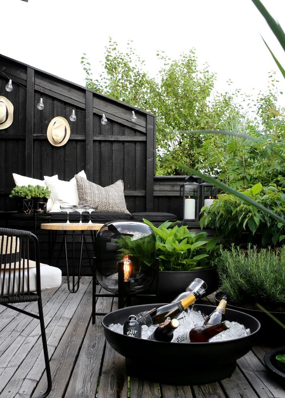 a Scandinavian balcony with black walls, a black built-in bench, a neutral hairpin leg table, black chairs and black pots with greenery