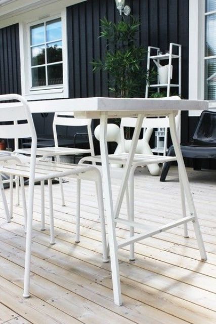 a Scandinavian terrace with a whitewashed deck, black plastic loungers and a black sofa, a white dining set and greenery
