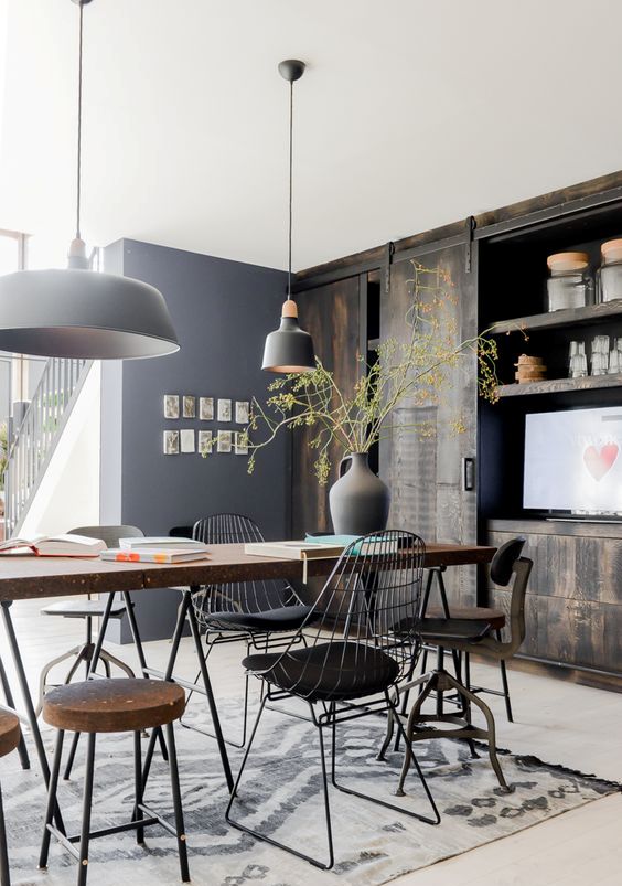 a beautiful rustic industrial dining space with a large table with a wood tabletop, mismatching chairs and stools, black pendant lamps and a reclaimed wood storage unit