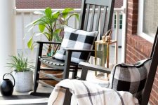 a black and white farmhouse porch with black rockers, checked textiles and a striped rug plus greenery