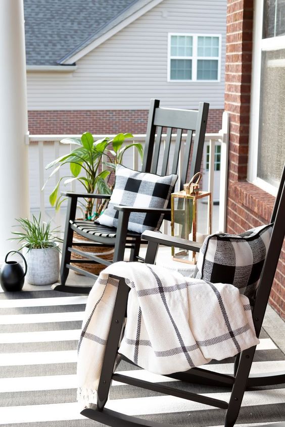 a black and white farmhouse porch with black rockers, checked textiles and a striped rug plus greenery