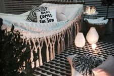 a black and white outdoor nook with a hammock, printed pillows, baskets with greenery, candles and candle lanterns