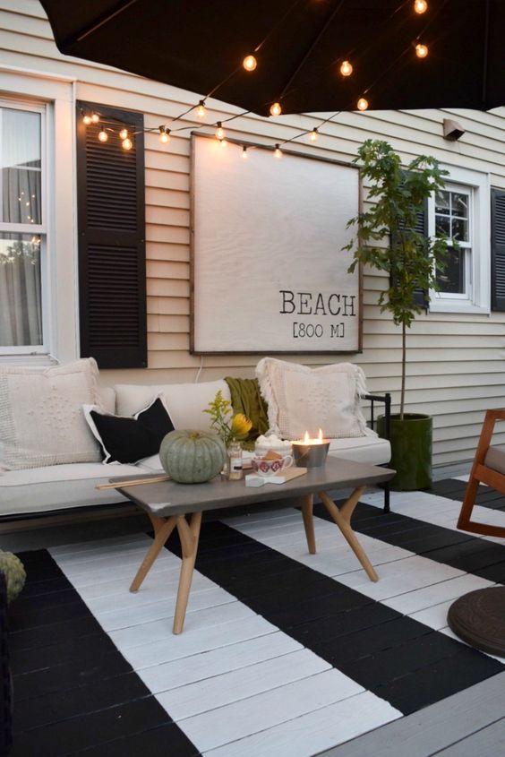 a black and white terrace with a painted deck, a black and white bench, a concrete table and lights over the space