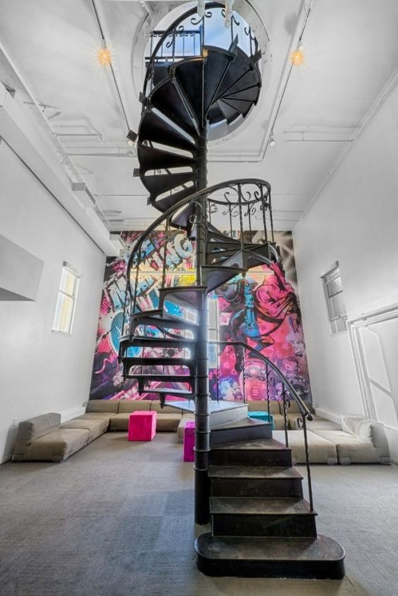 a bold and unique foyer with low grey and white sofas, a black forged staircase and a bold graffiti accent wall is a lovely space