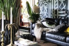 a bold living room with black and white graffiti on the wall, a black leather sofa, a black coffee table, brass candleholders and potted plants