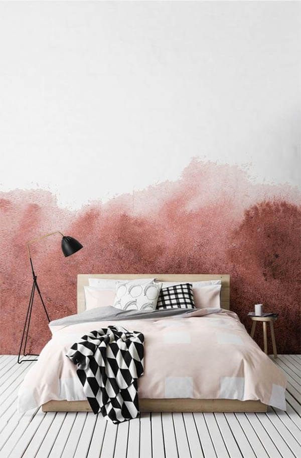a bright bedroom with a bold coral watercolor wall, a stained bed with printed bedding, a black floor lamp and a stool
