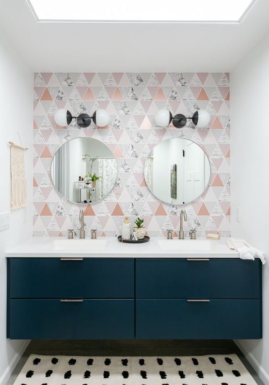 a catchy bathroom with a geo tile wall, a navy built in vanity and round mirrors plus vintage wall sconces