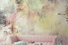 a catchy living room with a bold watercolor wall, a pink sofa, side tables with pastel vases and a gold chandelier