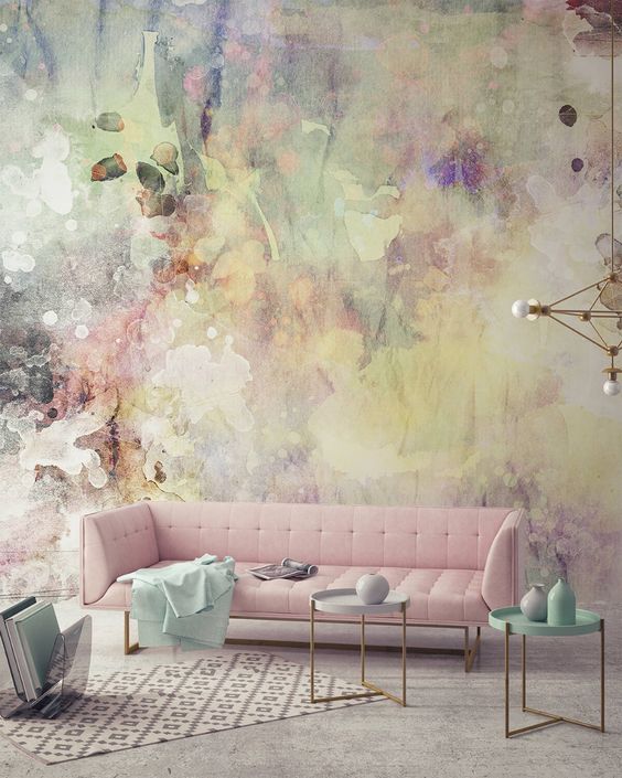 a catchy living room with a bold watercolor wall, a pink sofa, side tables with pastel vases and a gold chandelier