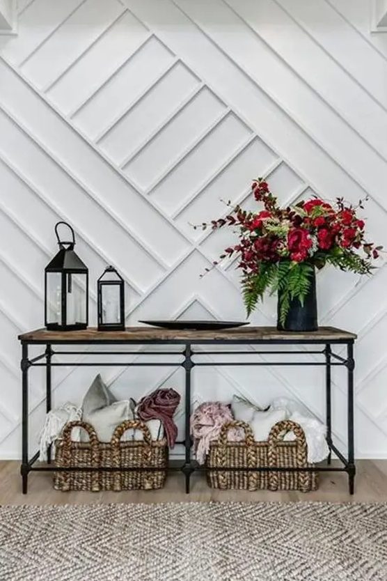 a chic entryway with a white paneled wall, an industrial console table, baskets with pillows and a bold floral arrangement